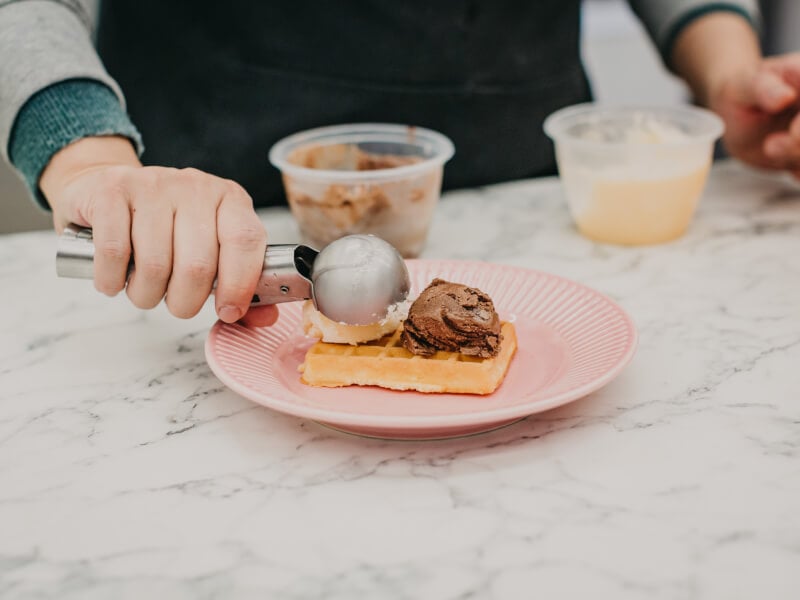 Ice cream being scooped onto a freshly baked waffle.